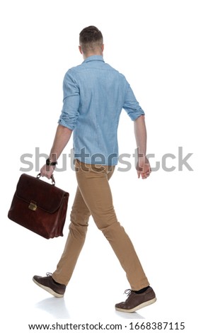 Side view of eager casual holding briefcase while wearing blue shirt, walking on white studio background