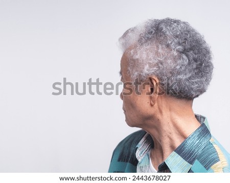 Side view of an elderly Asian woman with short white hair looking away while standing on a gray background. Space for text.