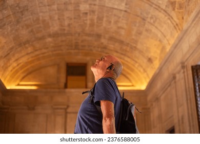 Side view of an elderly man admiring an ancient interior space of the Alhambra in Granada listening to information via audio guide, elderly man enjoying holidays and retirement in Europe