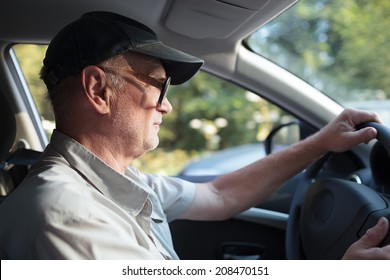 Side View Of An Elderly Man In Glasses Driving A Car On A Sunny Summer Day