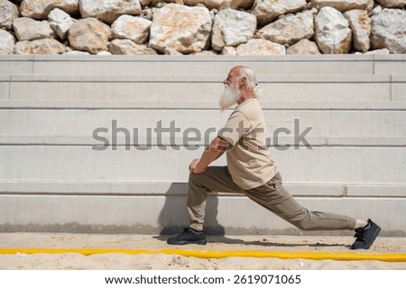 Side view of elderly man with long white beard doing lunge exerc