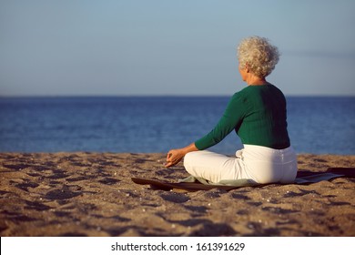 Side view of elderly woman in meditation on the beach. Senior lady sitting on the beach in lotus pose doing relaxation exercise. Old woman doing yoga. - Powered by Shutterstock