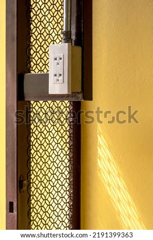 Side view of electrical power socket and conduit pipe line on edge of vintage steel door structure with yellow concrete wall in vertical frame