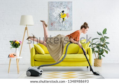 side view of elegant concentrated young woman levitating in air and vacuuming rug in living room
