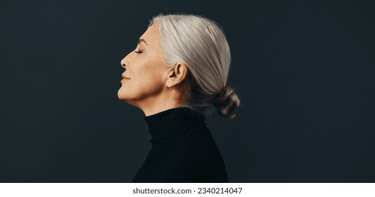 Side view of an empowered senior woman standing tall and confident in a studio setting, dressed in an elegant business attire and silver hair. - Powered by Shutterstock