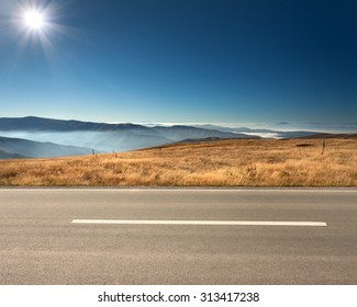 Side View Of Empty Asphalt Road And Cloudy Mountains In Background At Idyllic Sunny Day.