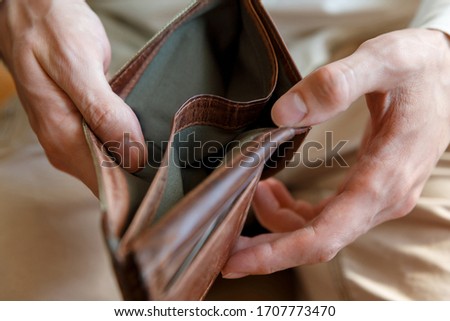 Side view of an empty wallet in the hands of a man on a light monophonic background. Bankruptcy and insolvency in the economy and finance. People have no money.