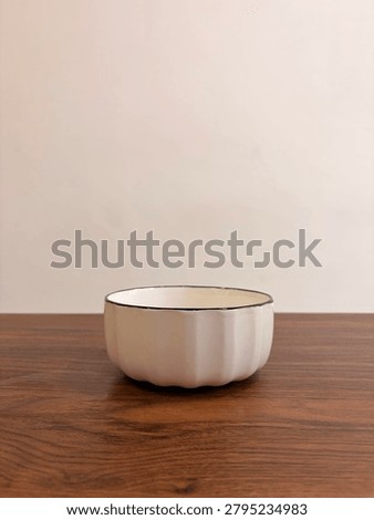 Side view of an empty white ceramic bowl with a black rim placed on a wooden table against a neutral background. 