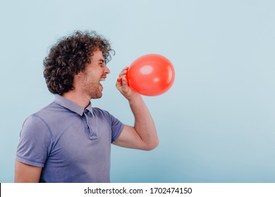 Side View Of Excited Casual Curly Man Closing Eyes And Laughing While Inhaling Helium Gas From Balloon Having Funny Voice