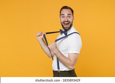 Side View Of Excited Cheerful Young Bearded Man 20s Wearing White Shirt Bow-tie Posing Standing Stretching Suspender Looking Camera Isolated On Bright Yellow Color Wall Background Studio Portrait