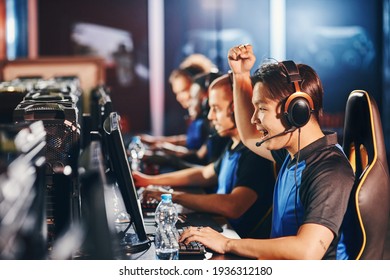 Side view of excited young asian guy, male cyber sport gamer looking at PC screen and raising hand up while - Shutterstock ID 1936312180