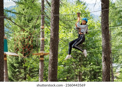 Side view of excited young female with opened mouth looking down while having fun on high ropes with belay cables protective helmet in forest adventure park in daylight - Powered by Shutterstock