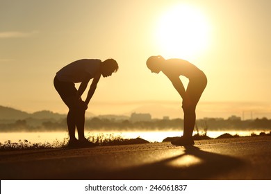 Side view of a exhausted and tired fitness couple silhouettes at sunset