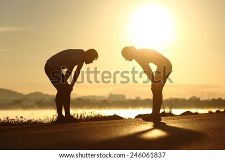Side view of a exhausted and tired fitness couple silhouettes at sunset