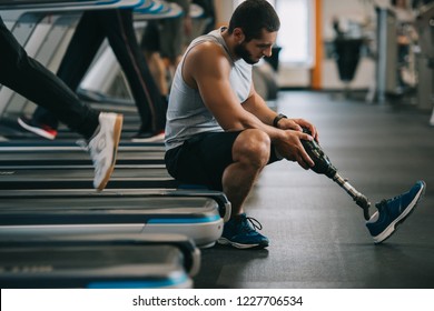 side view of exhausted young sportsman with artificial leg sitting on treadmill at gym - Powered by Shutterstock