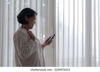 Side view: An expecting woman is talking on the phone next to glass window; smiling. - Shutterstock ID 2254976313