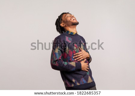 Side view extremely excited happy african guy with dreadlocks laughing holding his belly with hands, funny joke, anecdote. Indoor studio shot isolated on gray background