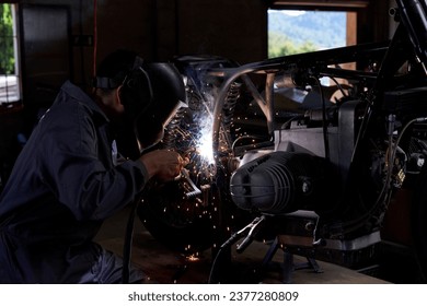 Side view of faceless mechanic wearing protective helmet and welding motorcycle in dark workshop