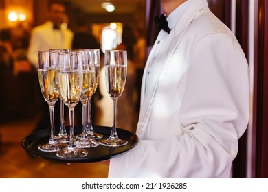 Side View Of Faceless Waiter In Uniform, Carrying Tray With Glasses Of Champagne During Wedding Party Against Blurred Background