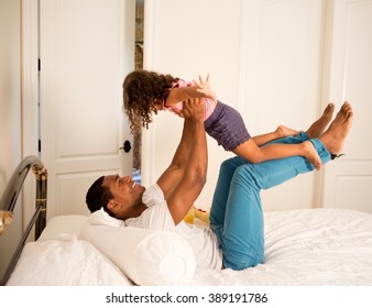 Side View Of Father Lying On Bed To Lifting Up Daughter, Face To Face Smiling