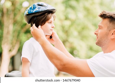 Side View Of Father Putting Helmet On Son While Boy Looking At Dad