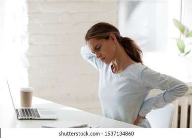 Side view fatigued young mixed race woman suffering from painful feelings in back due to long sedentary computer work at office or home. Unhealthy millennial female student having spine ache.