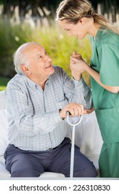 Side View Of Female Caretaker Helping Senior Man To Get Up From Couch