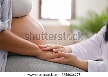 Side view of a female doctor reassuring and comforting a pregnant woman by touching or holding her hand. pregnancy medical checkup concept