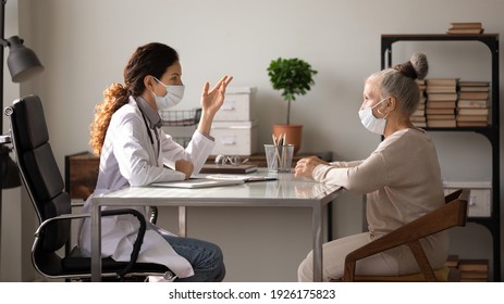 Side view female doctor wearing face mask and uniform consulting mature patient about treatment at meeting in hospital office, therapist and senior woman discussing checkup results, healthcare