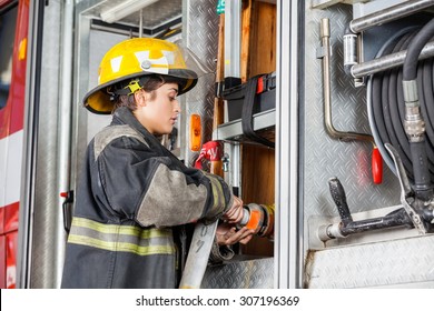 Side View Of Female Firefighter Fixing Water Hose In Truck At Fire Station