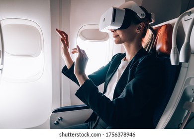 Side View Of Female In Formal Wear Entertaining With Virtual Reality Goggles And Exploring Air With Hands While Sitting In Cabin Of Aircraft