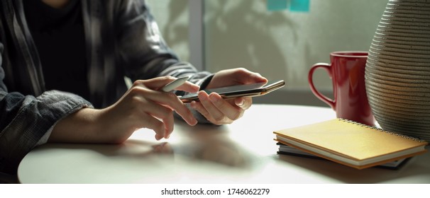 Side view of female freelancer using  smartphone while sitting at portable workspace beside window 