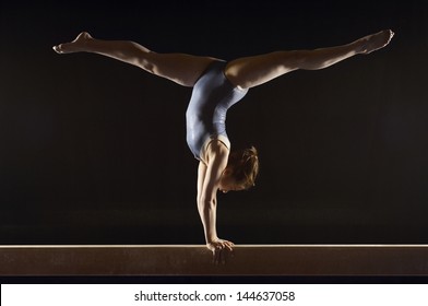 Side view of a female gymnast doing split handstand on balance beam against black background - Powered by Shutterstock