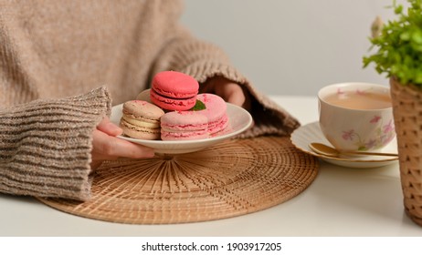 Side view of female hand holding a plate of French Colorful Macarons while having tea time in leisure corner - Powered by Shutterstock