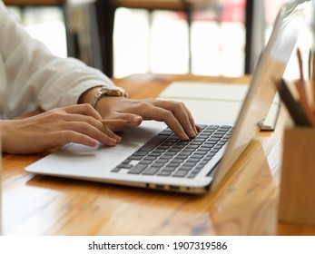 Side view of female hands typing on laptop keyboard and working with stationery on wooden table