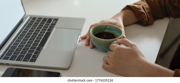 Side View Of Female Holding Coffee Cup While Looking On Mock Up Laptop On White Table With Smartphone