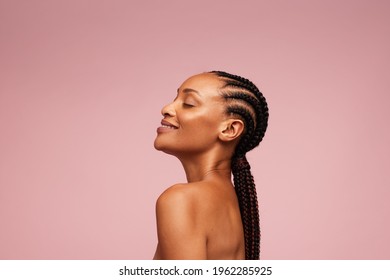 Side view of a female model having healthy and flawless skin. African american woman with braided hairstyle on pink background.