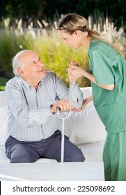 Side View Of Female Nurse Helping Senior Man To Get Up From Couch