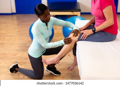 Side view of female physiotherapist giving leg massage to active senior woman in sports center. Sports Rehab Centre with physiotherapists and patients working together towards healing