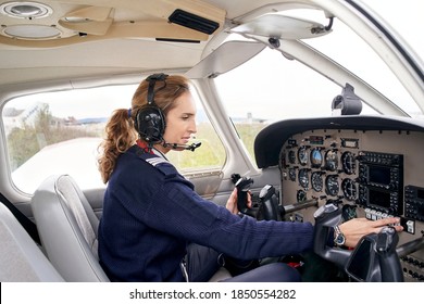 Side view of a female pilot in the cockpit of an airplane touching some buttons.