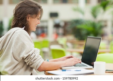 Side View Of A Female Student Using Laptop At Cafeteria Table