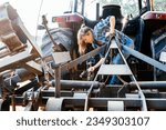 Side view of female technician in casual clothes repairing tractor with hammer on farm during daytime