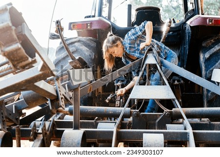 Side view of female technician in casual clothes repairing tractor with hammer on farm during daytime
