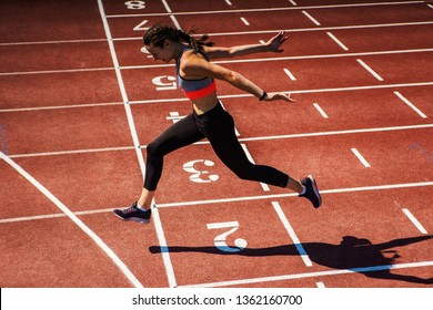 Side View Of Female Teen Athlete In Sports Bra And Tights Successfully Finishing Race On Track At Stadium 