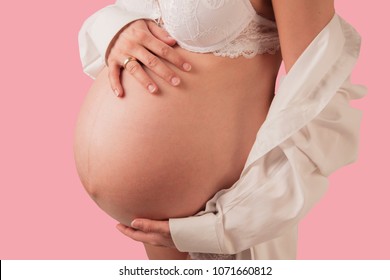 Side view of females pregnant belly. She covers her belly with her hands. The pink color background signalizes the female gender of the unborn child.