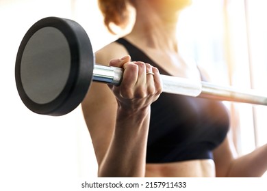 Side view of fit adult slim woman lifting barbell in fitness box. Close-up on the arm with muscles in front of the window. Workout at home or outdoors - Powered by Shutterstock