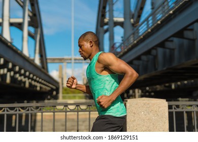 Side view of fit Black man in green tank top running down bridge during marathon training and breathing properly - Powered by Shutterstock