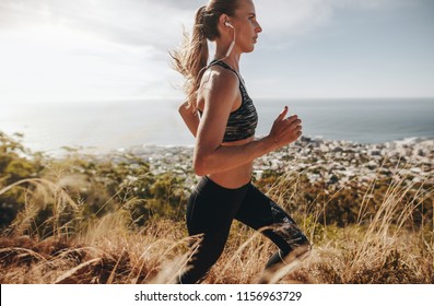 Side view of fit young woman wearing earphones running through mountain trail. Female runner training over rough trail in hillside. - Powered by Shutterstock