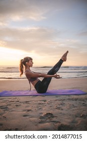 Side View Of Fit Young Woman Stretching And Doing Boat Yoga Pose On The Beach. Young Yogi Woman Practicing Yoga, Doing Paripurna Navasana Exercise.