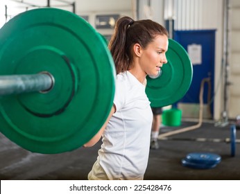 Side view of fit young woman lifting barbell in cross training box